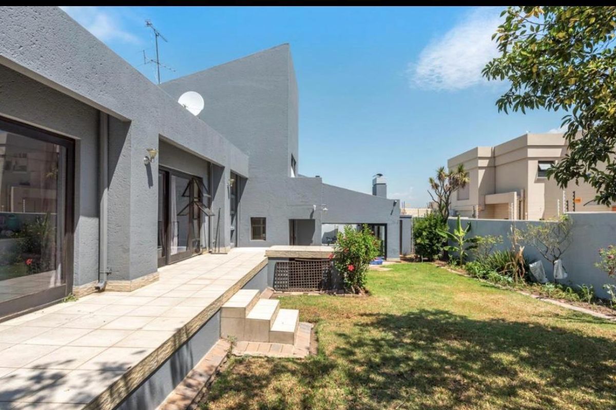 Rear view of the property featuring a tiled patio, concrete steps, and a private garden area with boundary walling.