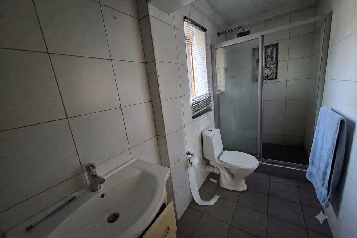A functional bathroom featuring a vanity basin, toilet, and a glass-enclosed shower with tiled finishes throughout.