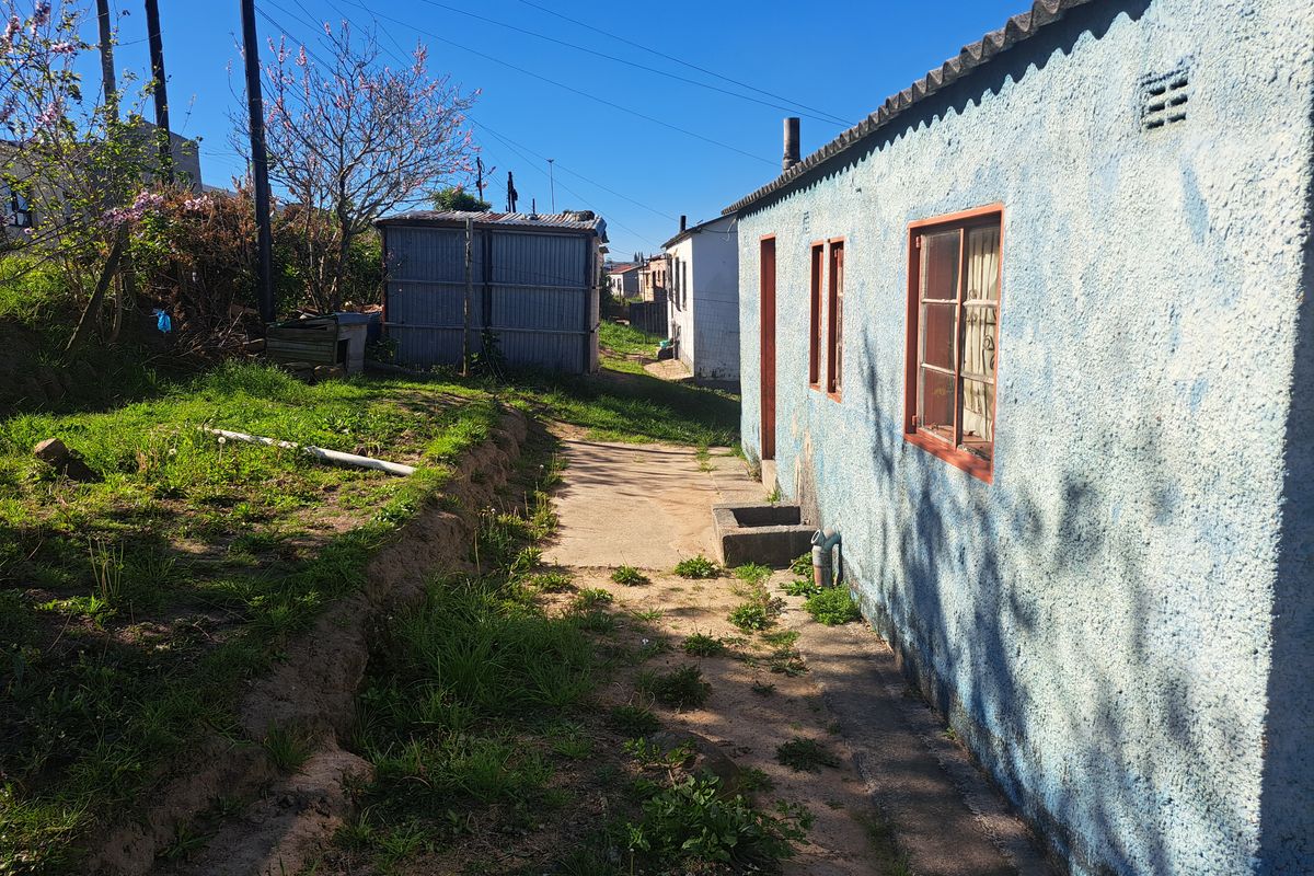 Rear exterior view of the property showing a textured masonry wall, timber-framed windows, and a concrete pathway leading to the backyard area.