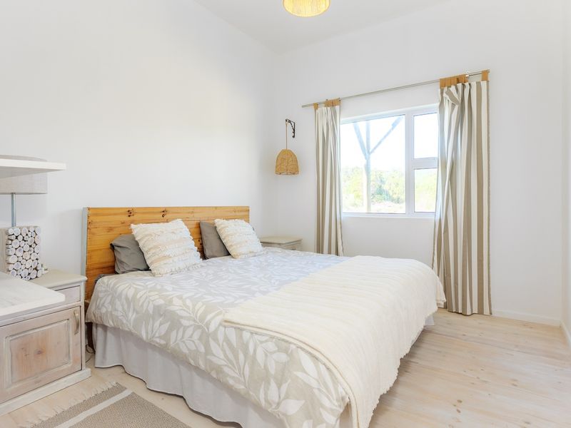 A bright and well-maintained bedroom featuring neutral finishes, a built-in shelving unit, and a window providing natural light.