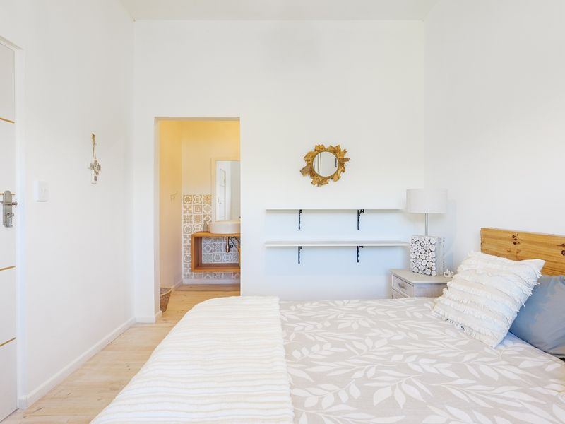 A bright bedroom featuring light laminate flooring, built-in wall shelving, and direct access to an en-suite bathroom with decorative tiling.