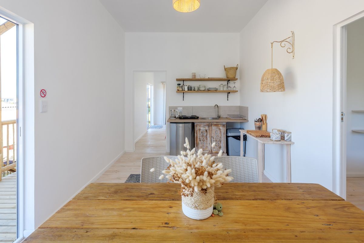 A compact kitchenette featuring wooden cabinetry, open shelving, and a sink, with direct access to an outdoor timber deck.