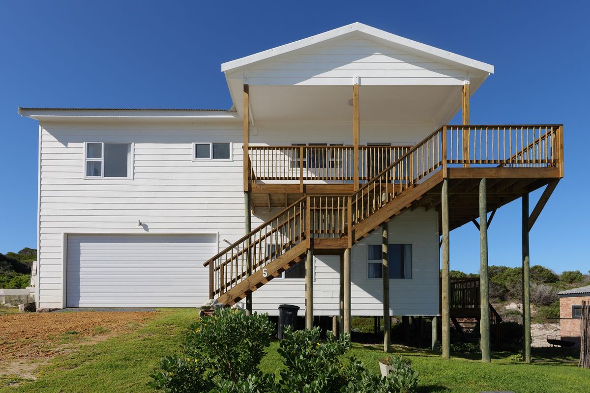 Rear view of a two-story house featuring white weatherboard cladding, a raised timber deck with stairs, and an integrated garage.