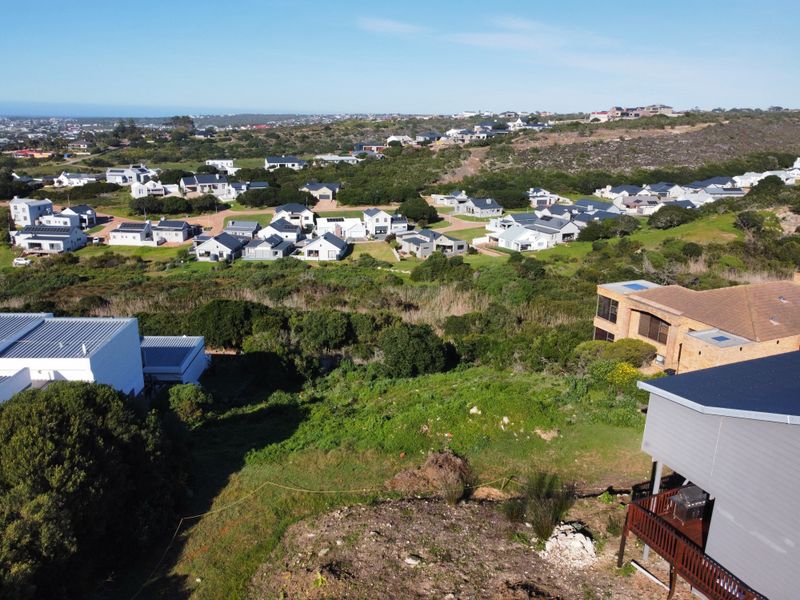 An aerial view of a vacant residential plot situated within a developed coastal estate, surrounded by established homes and natural vegetation.