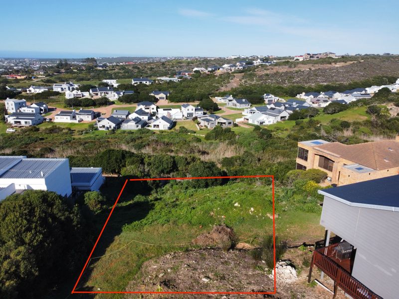 An aerial view of a vacant residential plot marked with red boundary lines, situated in a developed coastal neighborhood.