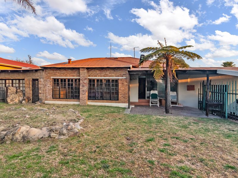 Rear view of a brick house featuring a corrugated metal roof, timber-framed windows, and a paved patio area overlooking a garden.