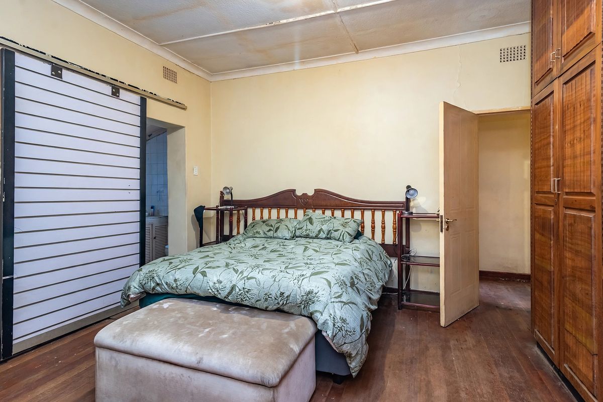 A bedroom featuring built-in wooden cupboards and timber flooring, requiring cosmetic updates and ceiling repairs to restore its condition.