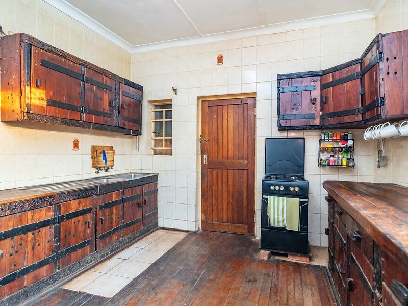 A rustic kitchen featuring wooden cabinetry, tiled walls, and a freestanding stove, offering a dated aesthetic with potential for modernization.