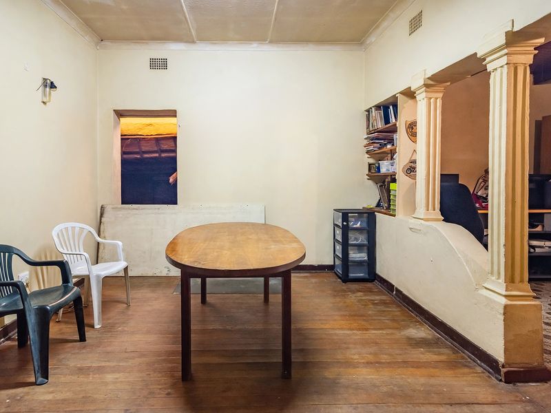 A dining area featuring timber flooring, decorative columns, and built-in shelving, offering a dated space with potential for modernization.