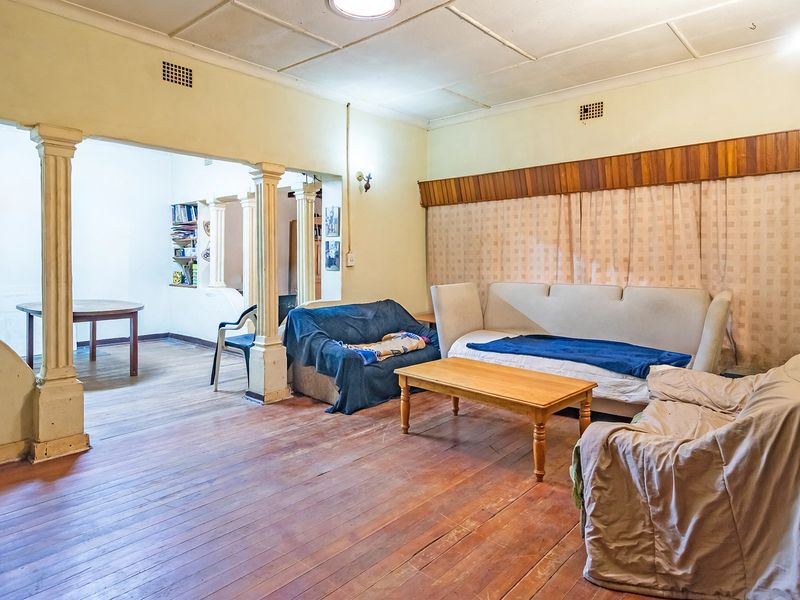 Spacious living area featuring original hardwood flooring, decorative columns, and timber wall paneling, offering a classic layout with potential for modernization.
