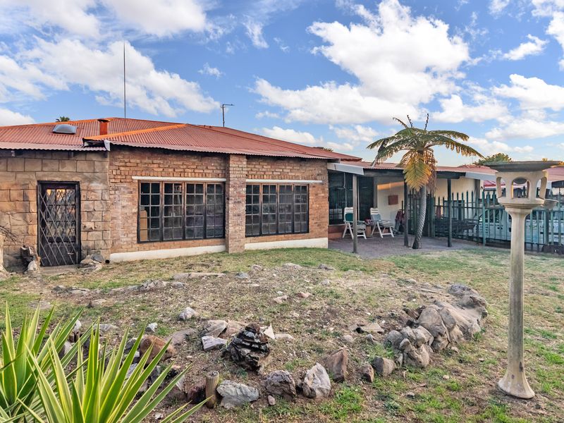 Rear view of the property featuring a brick and stone facade, corrugated metal roof, and a covered patio area overlooking the garden.
