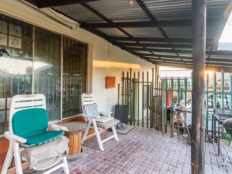 A covered outdoor patio area featuring paved flooring, a corrugated metal roof, and secure metal gate access to the property exterior.