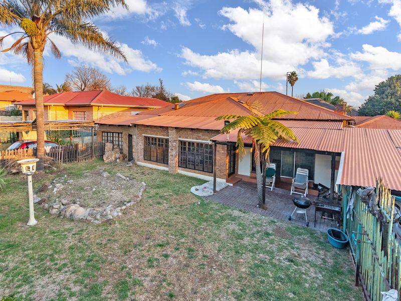 Rear view of the property featuring a brick facade, corrugated metal roof, and a paved patio area with a covered veranda.