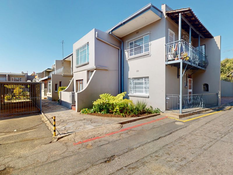 Front exterior view of a townhouse complex featuring paved driveway, carport, and upper-level balcony with security bars.