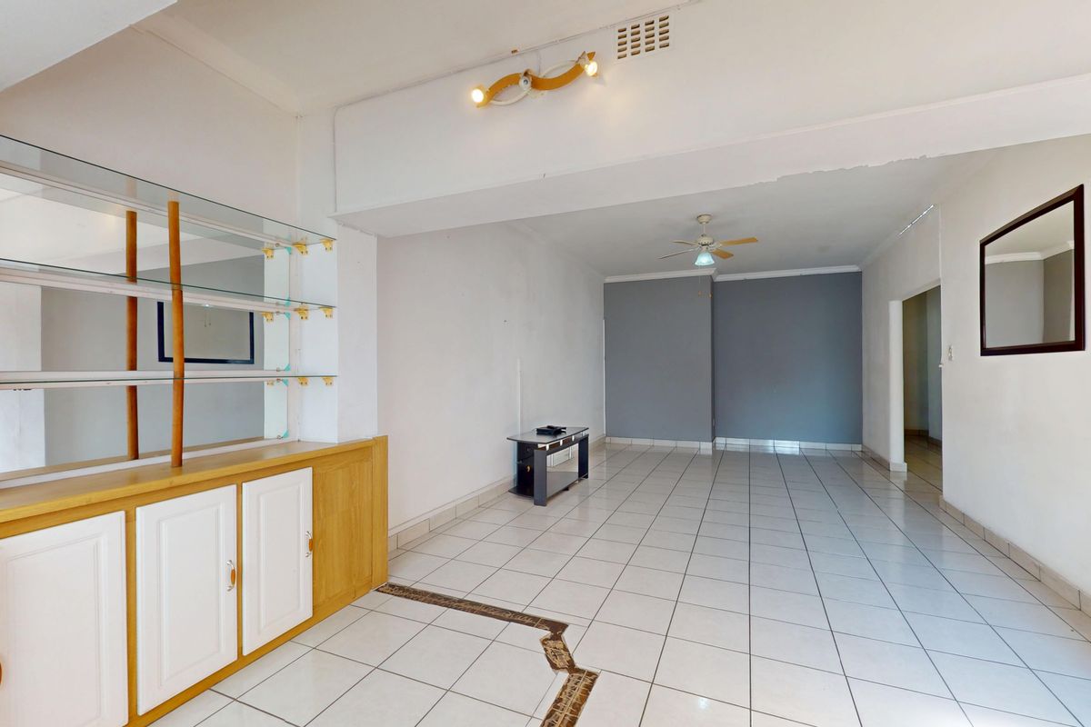 Spacious open-plan living area featuring tiled flooring, built-in cabinetry, and a ceiling fan, offering a blank canvas for renovation.