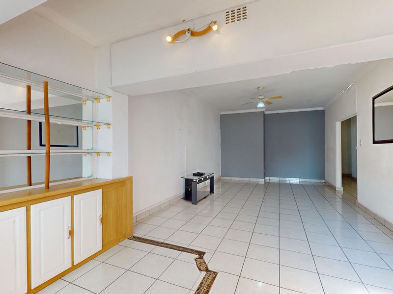 Spacious open-plan living area featuring tiled flooring, built-in cabinetry, and a ceiling fan, offering a blank canvas for renovation.