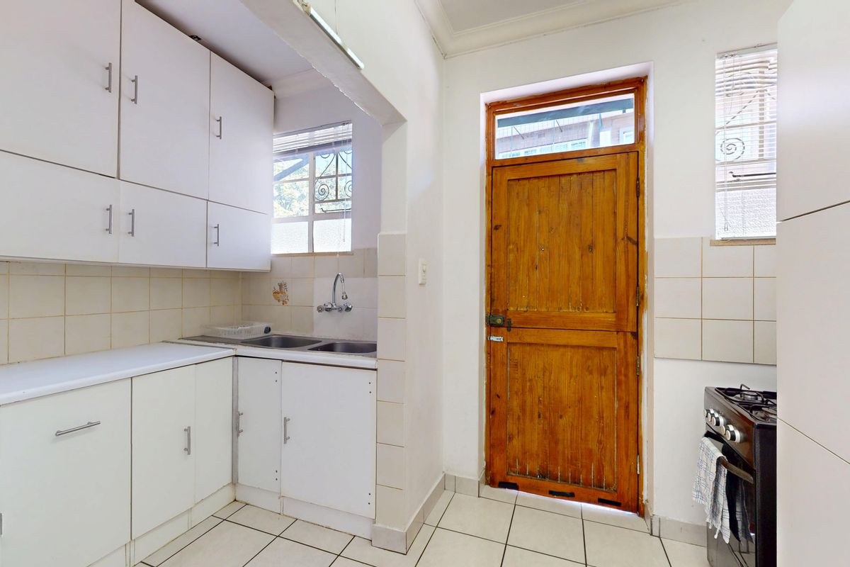 Functional kitchen featuring white built-in cabinetry, tiled splashbacks, double sink, and a timber door leading to the exterior.