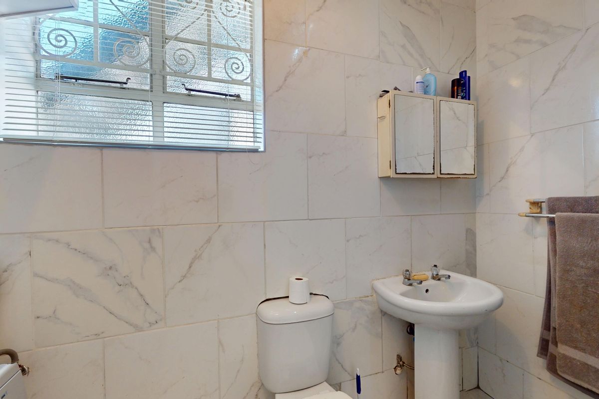 A functional bathroom featuring marble-look wall tiles, a pedestal basin, a toilet, and a wall-mounted medicine cabinet with a window for natural light.
