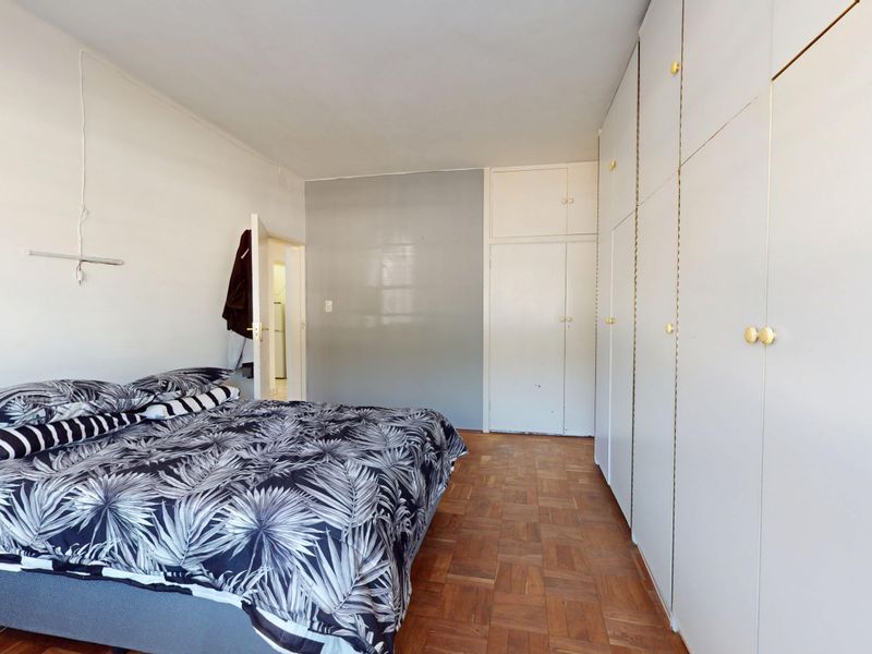 A bedroom featuring classic parquet flooring and extensive built-in cupboard storage, offering a functional layout with neutral wall finishes.