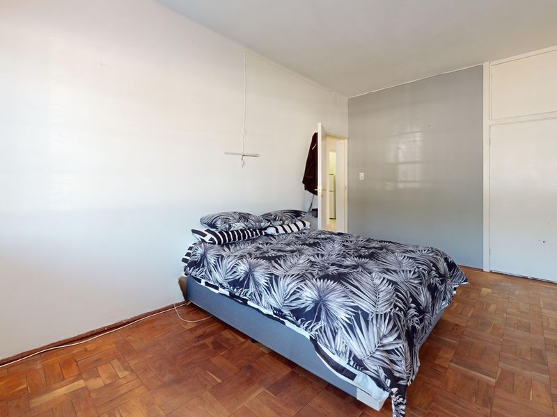 A bedroom featuring classic parquet flooring and integrated built-in cupboards, offering a functional space with potential for cosmetic updates.