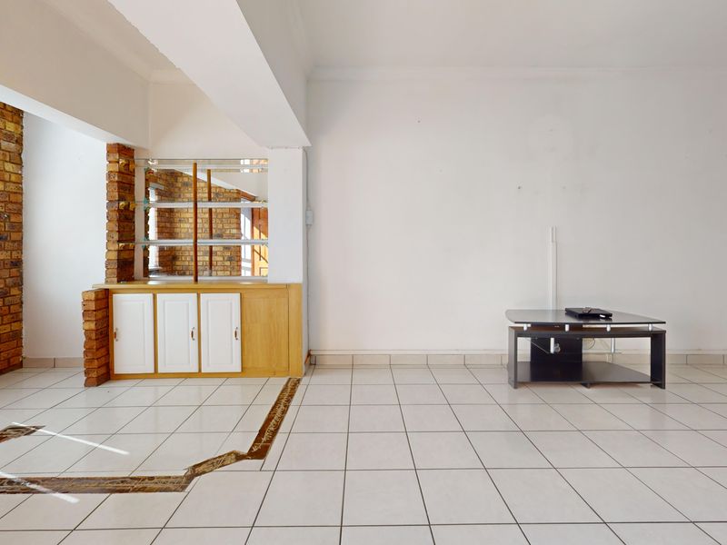 An empty living room featuring exposed brickwork, built-in cabinetry, and ceramic tiled flooring with a decorative inlay detail.