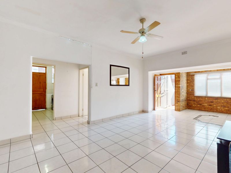 Spacious living area featuring tiled flooring, a ceiling fan, and an exposed brick feature wall, offering a bright and open layout.