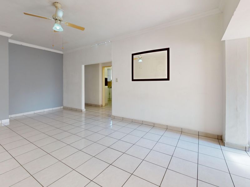 A spacious, empty living area featuring neutral ceramic floor tiles, a ceiling fan, and a clean, minimalist aesthetic ready for personalization.
