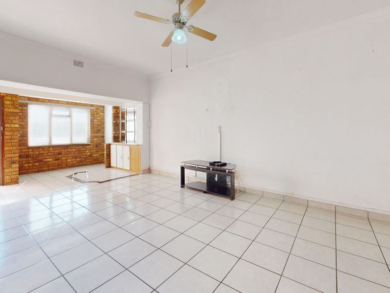 Spacious living area featuring tiled flooring, a ceiling fan, and an exposed brick accent wall with built-in cabinetry.