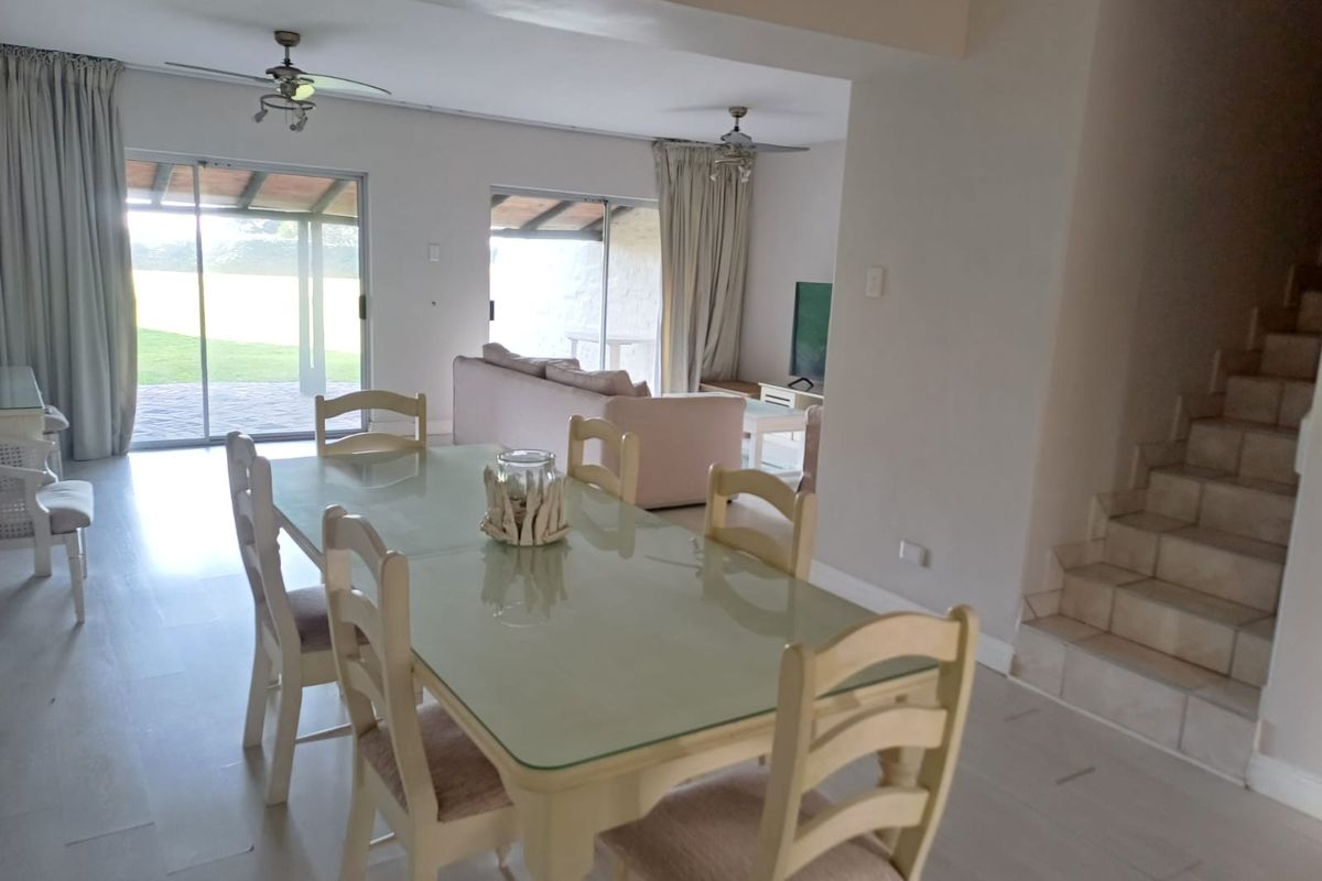 Open-plan dining and living area featuring tiled flooring, ceiling fans, and large sliding glass doors providing access to the outdoor patio and garden.