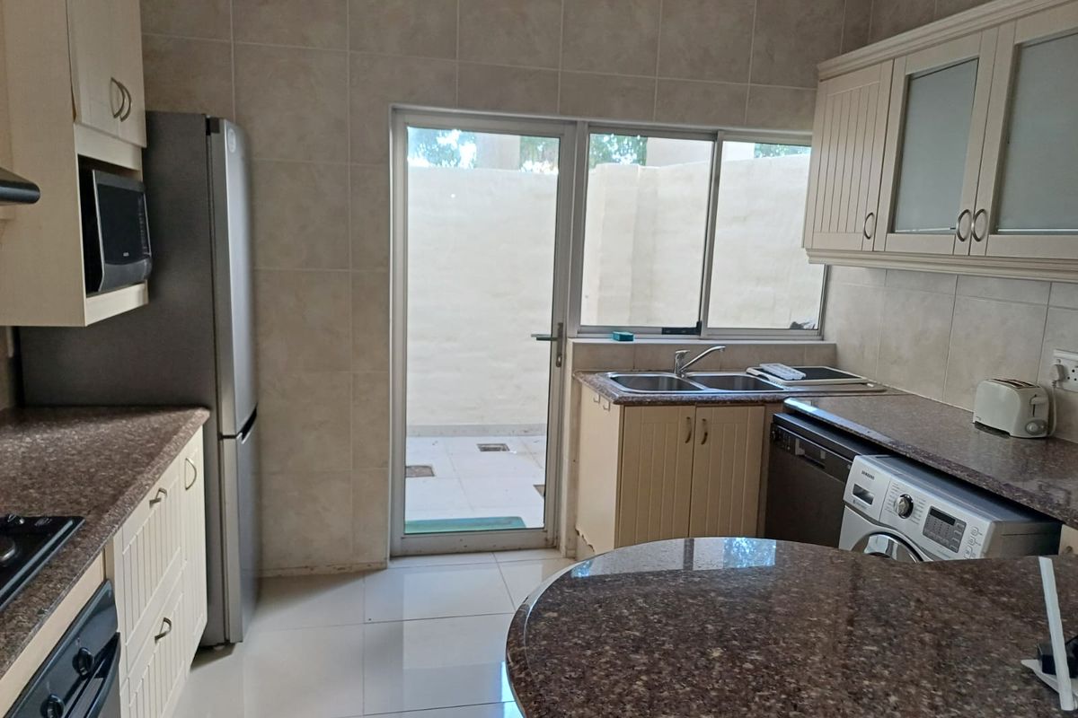 A functional kitchen featuring granite countertops, built-in cabinetry, tiled finishes, and direct access to an outdoor patio area.