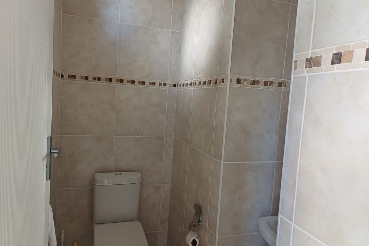A compact guest bathroom featuring floor-to-ceiling ceramic tiling with a decorative mosaic border, equipped with a standard toilet and pedestal basin.