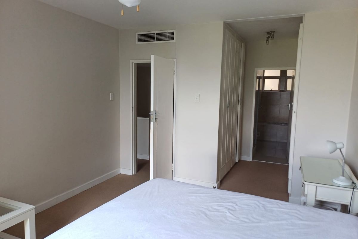 A bedroom featuring built-in cupboards, carpeted flooring, and a ducted air conditioning vent, with direct access to an en-suite bathroom.