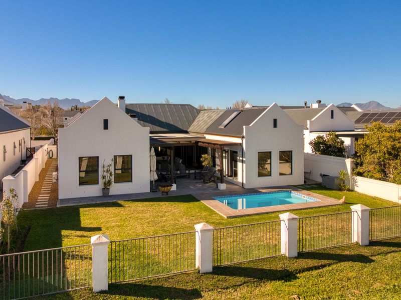 Rear view of a modern house featuring a swimming pool, paved patio area, well-maintained lawn, and perimeter fencing with mountain views in the background.