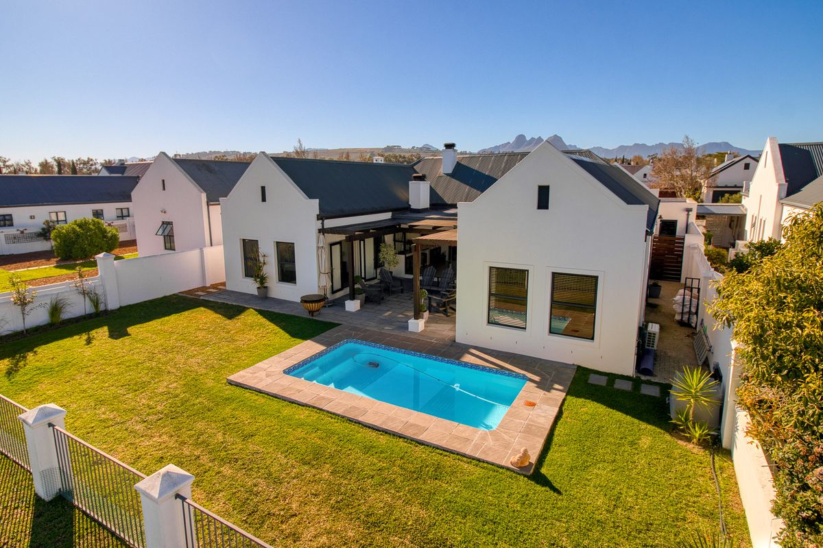 Aerial view of the rear exterior featuring a well-maintained garden, a swimming pool with paved surround, and a covered patio area with a pergola.