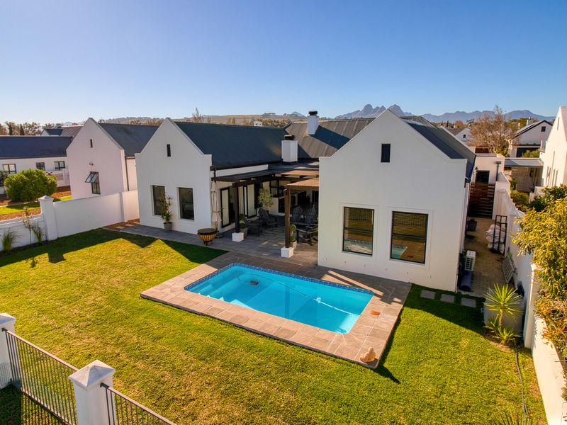 Aerial view of the rear exterior featuring a well-maintained garden, a swimming pool with paved surround, and a covered patio area with a pergola.