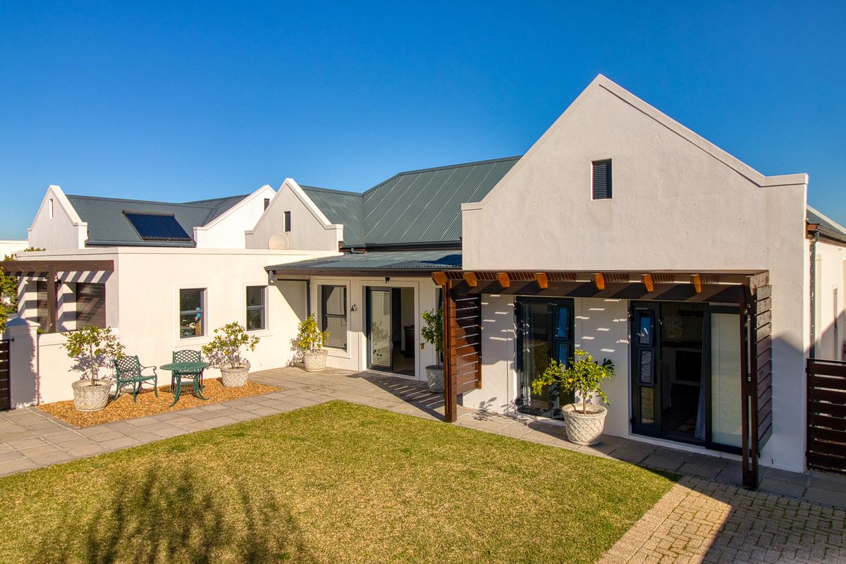A well-maintained rear exterior view featuring a paved patio, timber pergola, lawn, and modern metal roofing with integrated solar water heating.