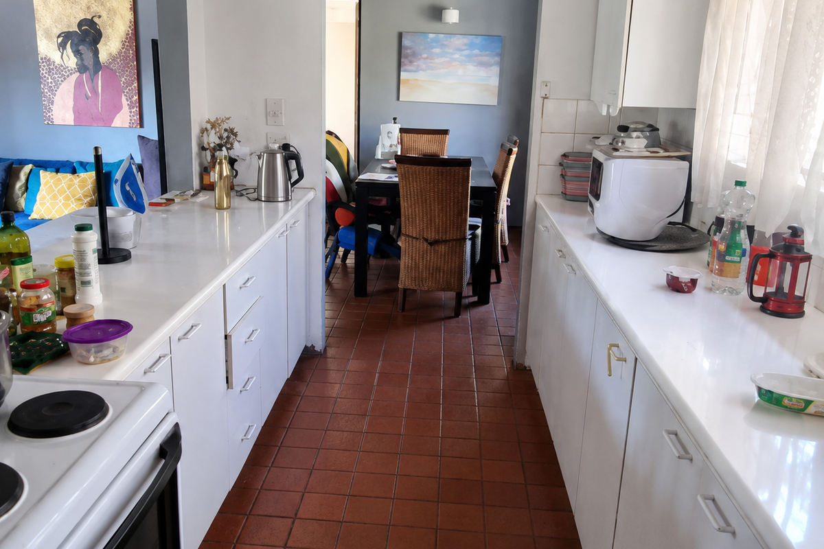 A functional galley-style kitchen featuring white cabinetry, tiled flooring, and an electric stove, with an open-plan flow leading into the dining area.