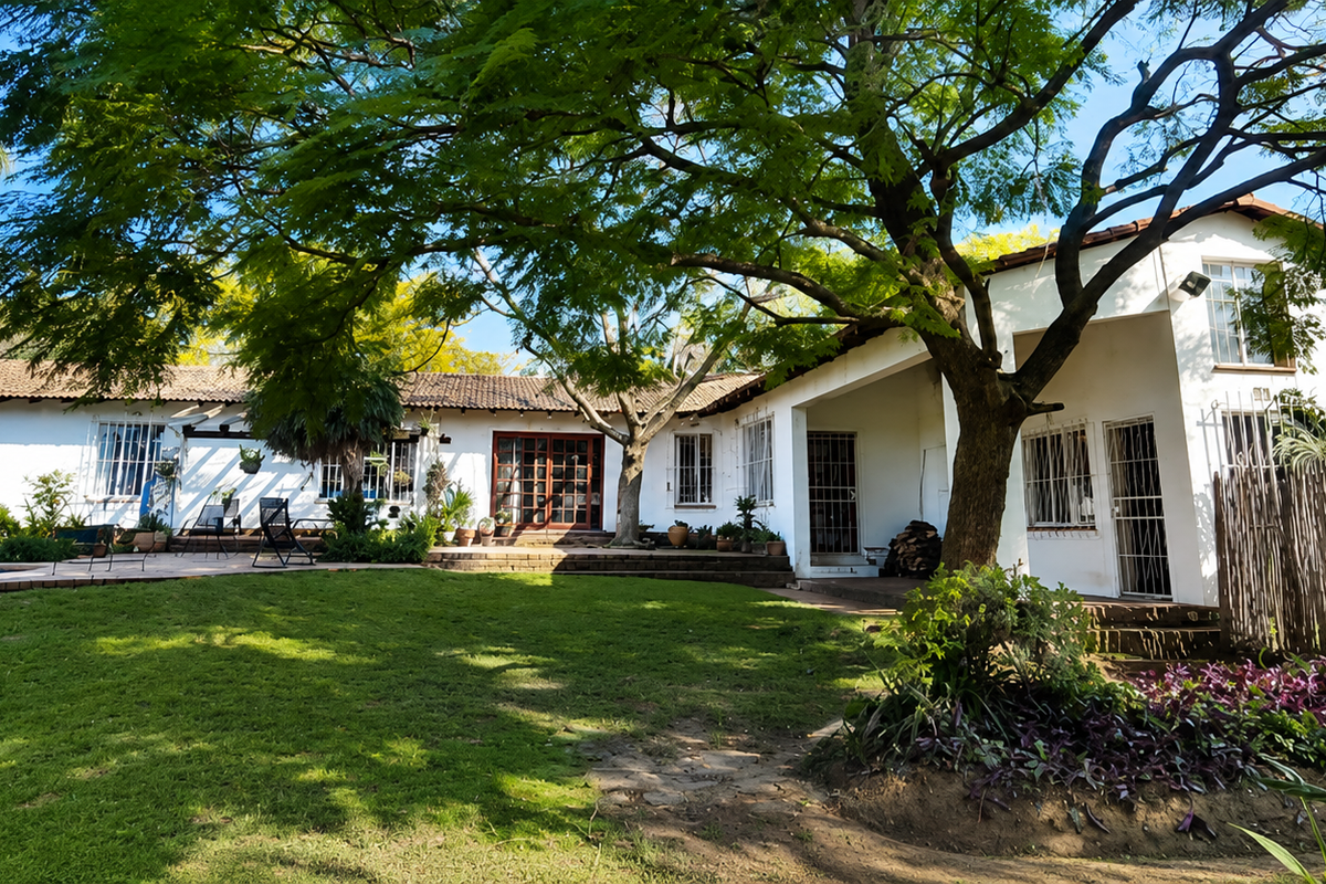 Rear view of the small holding featuring a white-walled residence, a swimming pool, mature trees, and a landscaped garden area.