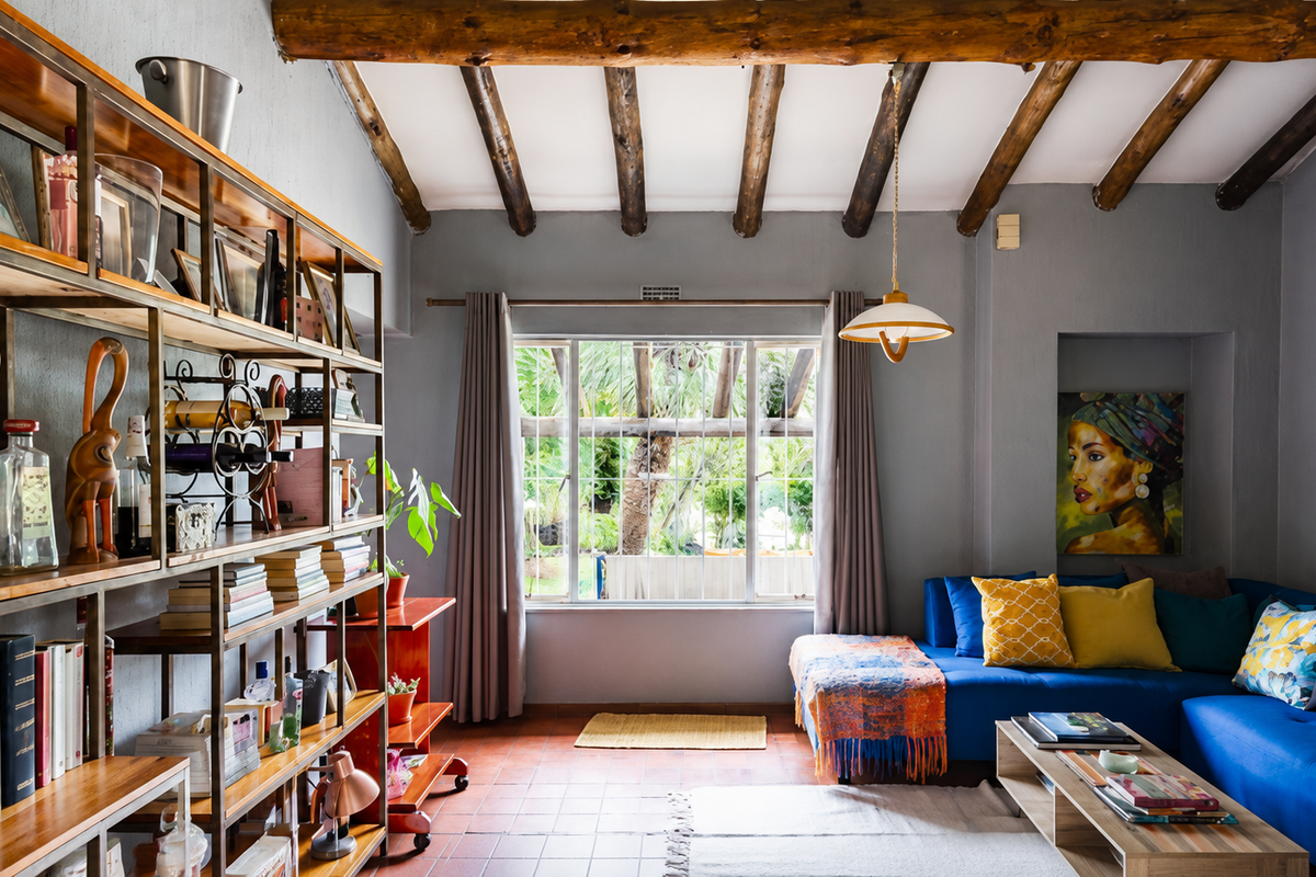A cozy living room featuring exposed timber ceiling beams, terracotta floor tiles, and a large window overlooking the garden.