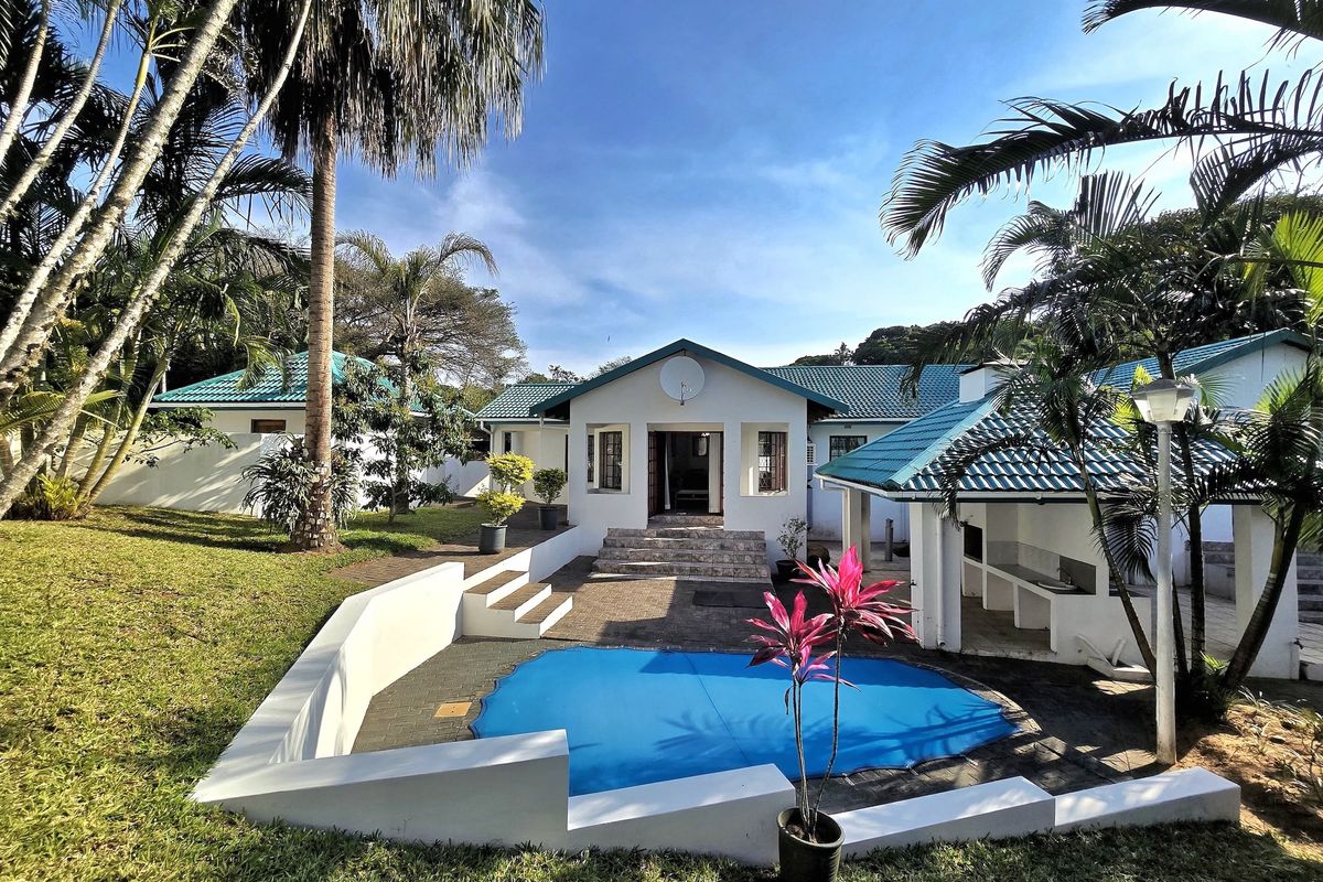 Rear view of the property featuring a swimming pool, paved patio area with a built-in braai, and well-maintained garden surroundings.