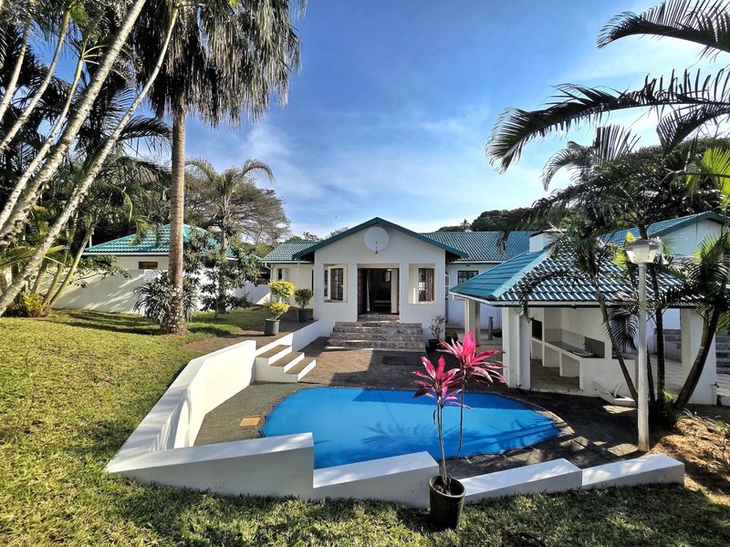 Rear view of the property featuring a swimming pool, paved patio area with a built-in braai, and well-maintained garden surroundings.