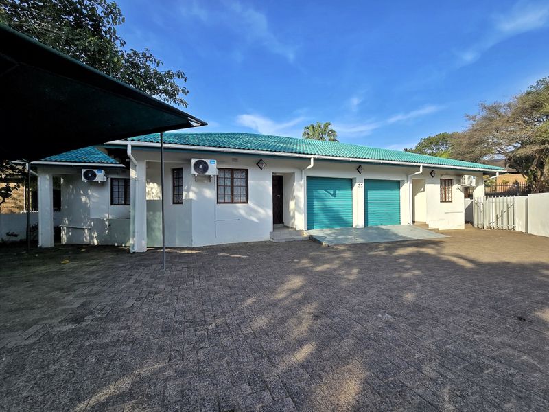 Front elevation of a residential property featuring a double garage, paved driveway, and tiled roof with installed air conditioning units.