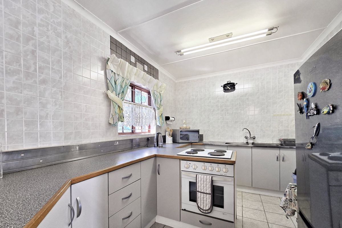 A functional kitchen featuring built-in cabinetry, laminate countertops, an electric stove with oven, and tiled splashbacks, offering a practical layout for daily use.