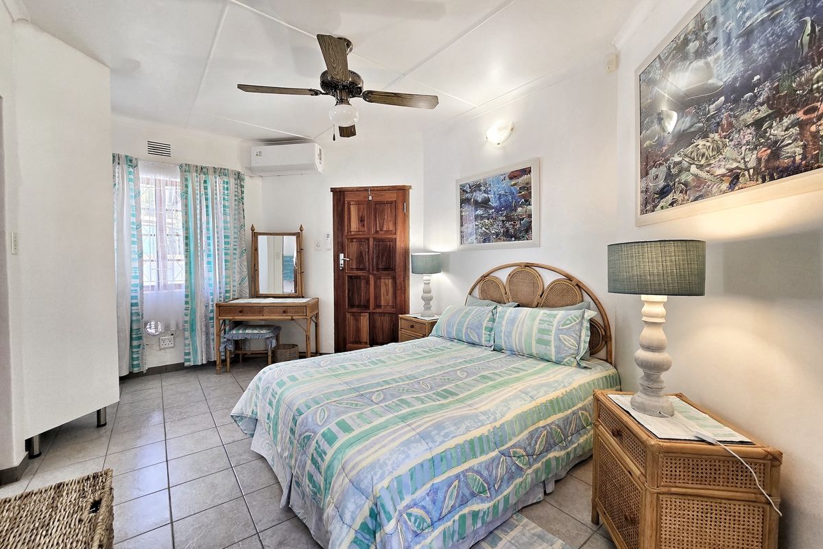 A well-lit bedroom featuring tiled flooring, a ceiling fan, and a wall-mounted split-system air conditioner.