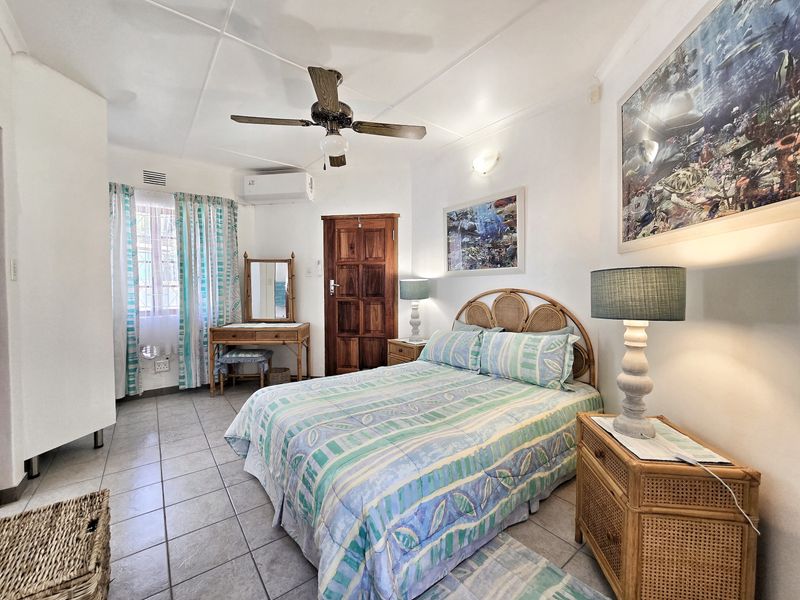 A well-lit bedroom featuring tiled flooring, a ceiling fan, and a wall-mounted split-system air conditioner.