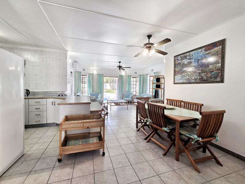 Spacious open-plan living and dining area featuring tiled flooring, ceiling fans, and a functional kitchen layout with direct access to the outdoor pool area.