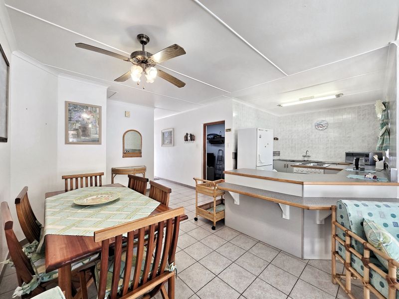 Open-plan living and dining area featuring a functional kitchen with breakfast bar, tiled flooring, and a ceiling fan.