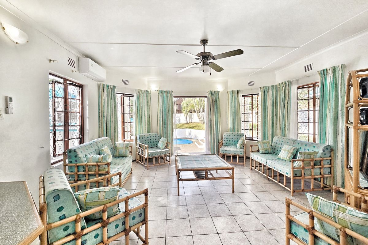 Spacious living room featuring tiled flooring, a ceiling fan, air conditioning, and large windows with security bars, offering direct access to the outdoor pool area.