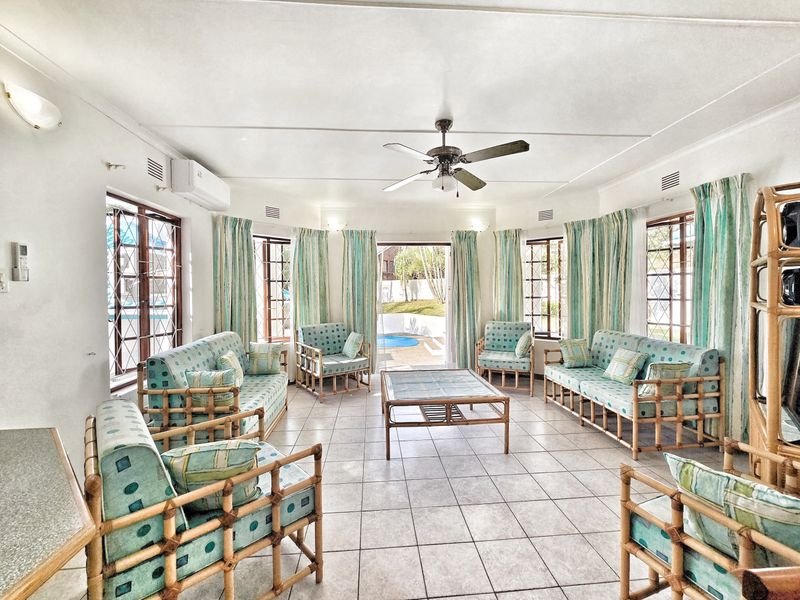 Spacious living room featuring tiled flooring, a ceiling fan, air conditioning, and large windows with security bars, offering direct access to the outdoor pool area.