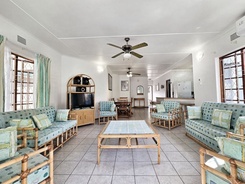 Spacious open-plan living and dining area featuring tiled flooring, ceiling fans, and a breakfast bar connecting to the kitchen.